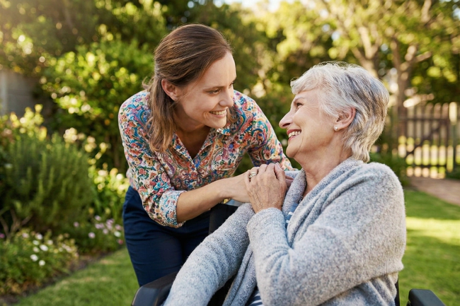 Eine Pflegekraft, die über eine Pflegeagentur angestellt ist, um eine ältere, rollstuhlpflichtige Frau zu betreuen.